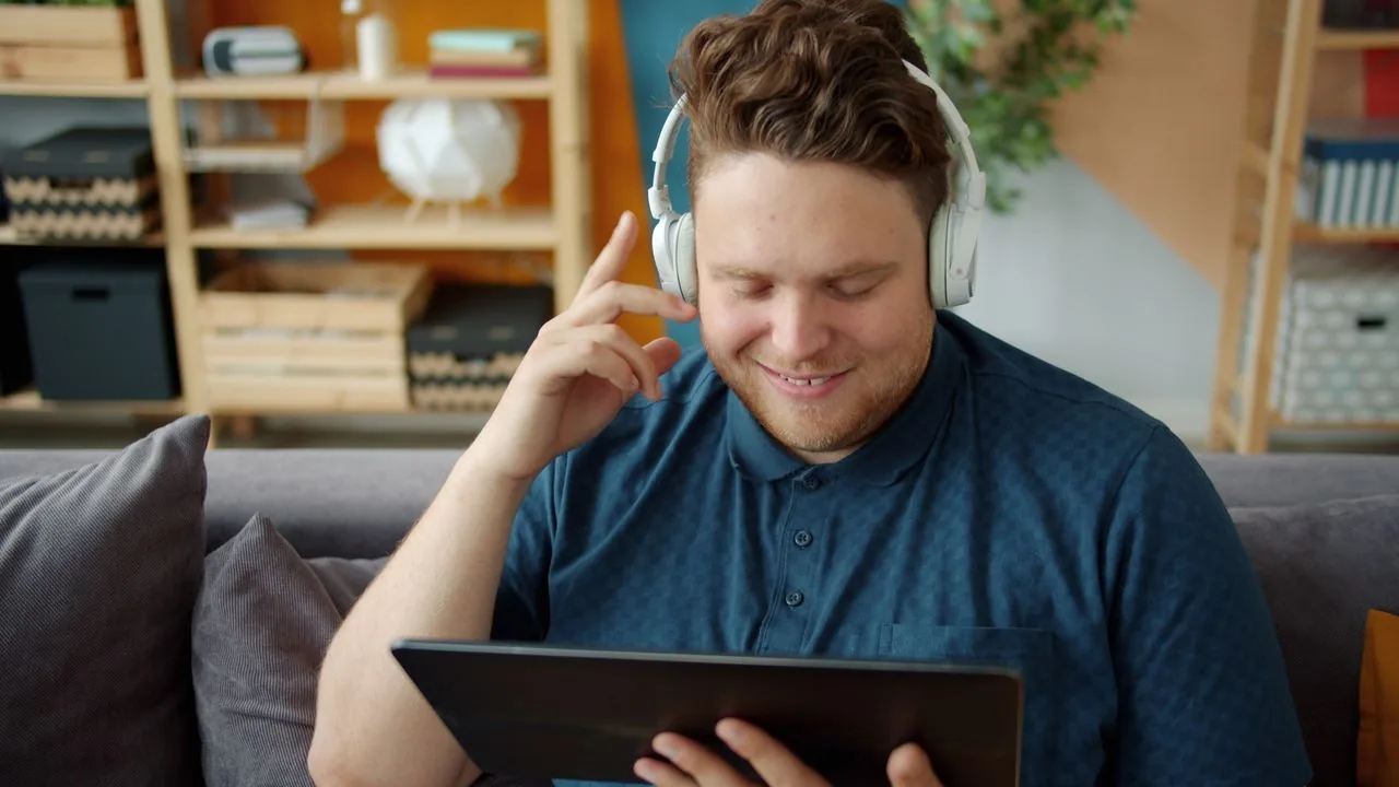Man wearing wireless Bluetooth headphones while watching a video on a tablet at home