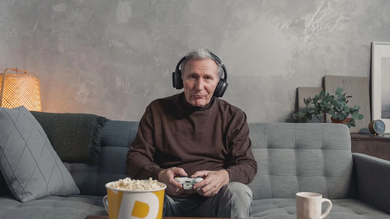 Man wearing wireless Bluetooth headphones holding a game controller on a sofa