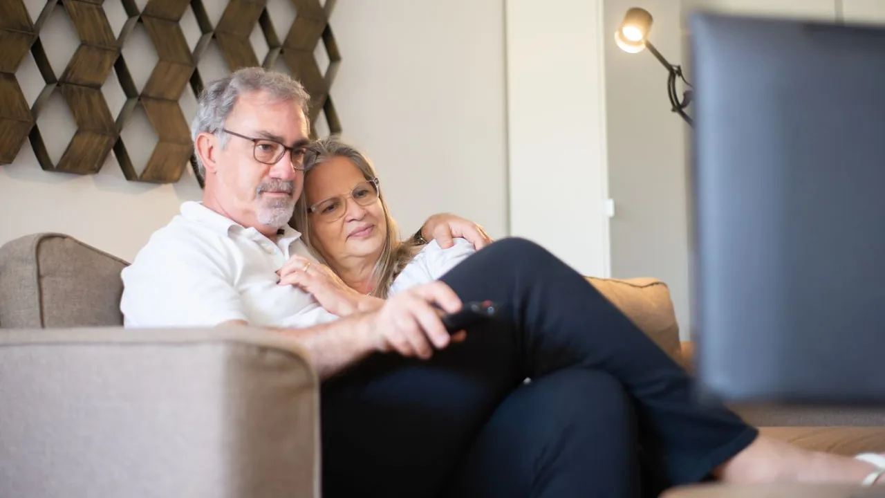 Couple sitting on a sofa with a remote control in front of a television at home
