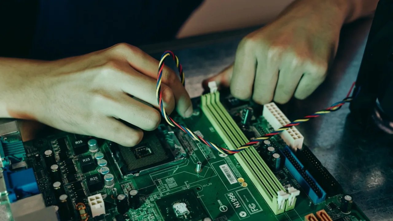 Hands working inside a desktop computer next to the motherboard's memory slots