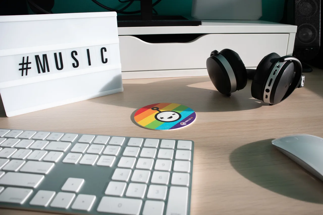 Keyboard, mouse and over-ear headphones on a wooden desk with speakers and a monitor