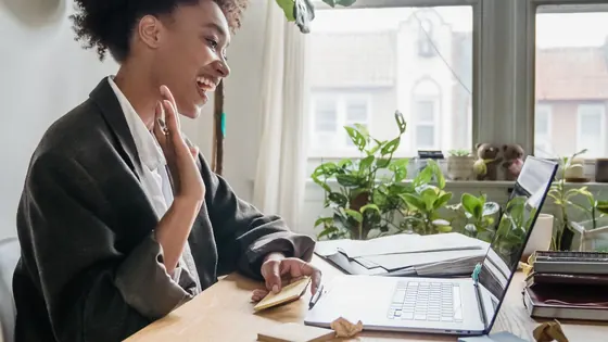 Smiling woman waving at her laptop during a video call at a bright home office desk