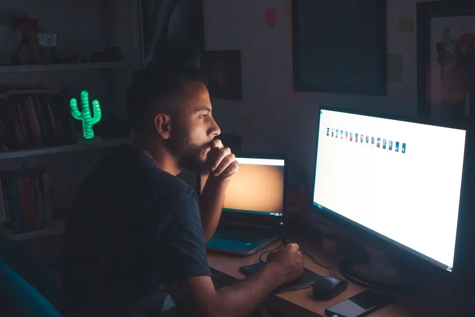 Man working at a computer in a dark room lit mostly by the monitor glow