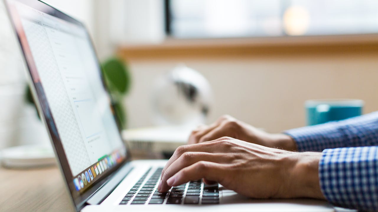 Person typing on a MacBook laptop keyboard — laptop keyboards commonly ghost on 3+ key combinations