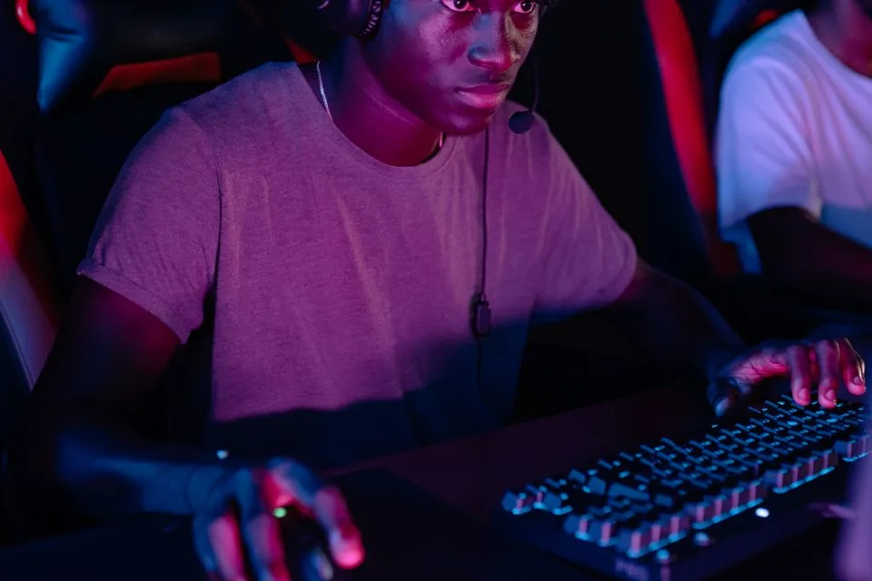 Focused player wearing a headset at a dark esports desk with one hand on the mouse and one on a backlit keyboard