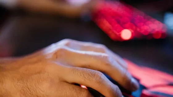 Hand gripping a gaming mouse on a dark cloth mousepad beside a red backlit keyboard, about to make a fast flick