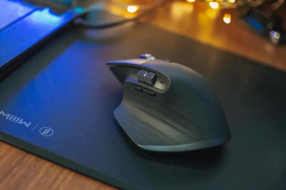 Wireless mouse resting on a large black cloth mousepad on a wooden desk with warm lights in the background
