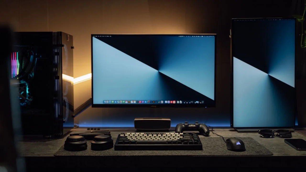 A dim desk with monitors running an even, full-screen moving pattern, the kind of pixel-refresher cycle used to clear temporary OLED image retention