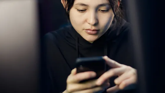 Woman looking intently at her smartphone in a dimly lit room, checking why it did not vibrate