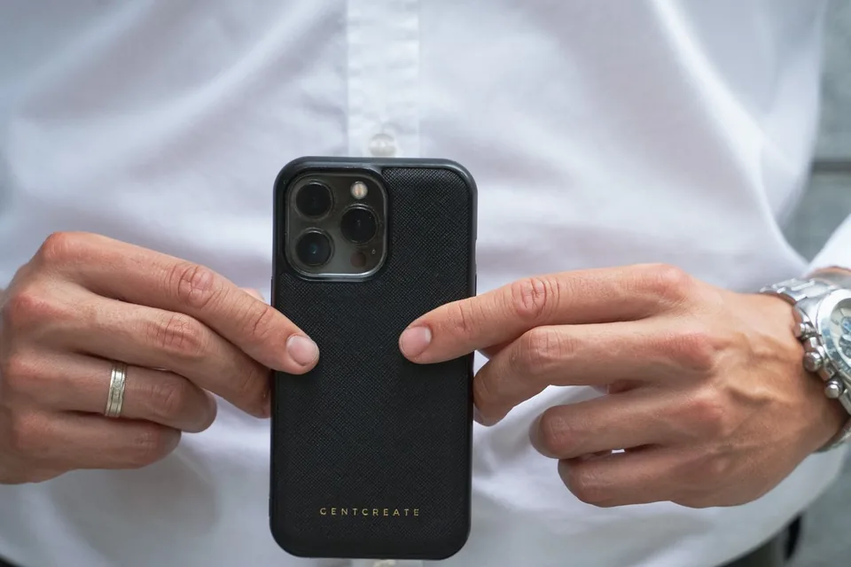 Hände halten ein Smartphone in einer dicken schwarzen Schutzhülle und zeigen auf die Rückseite der Hülle