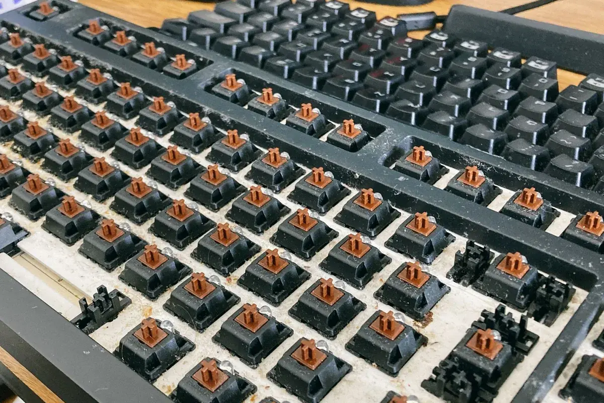 A keyboard with keycaps removed showing dust and debris underneath, the common cause of a sticky spacebar