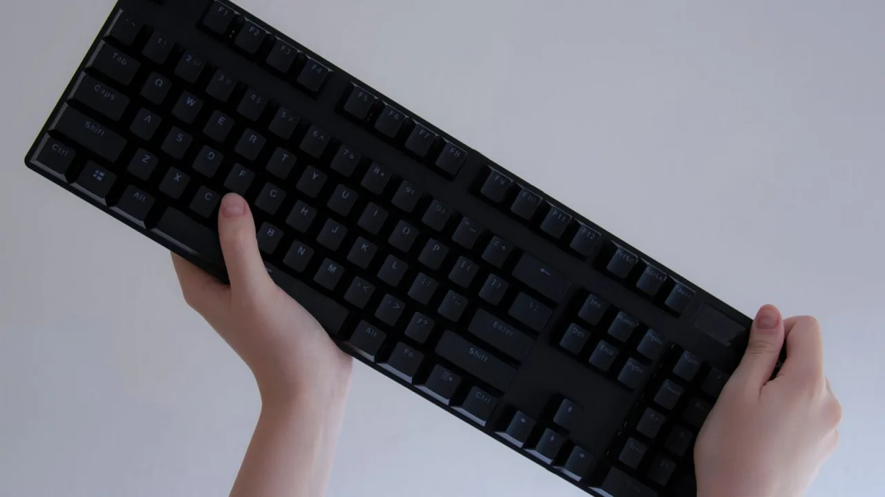 Two hands lifting a black keyboard against a plain bright background