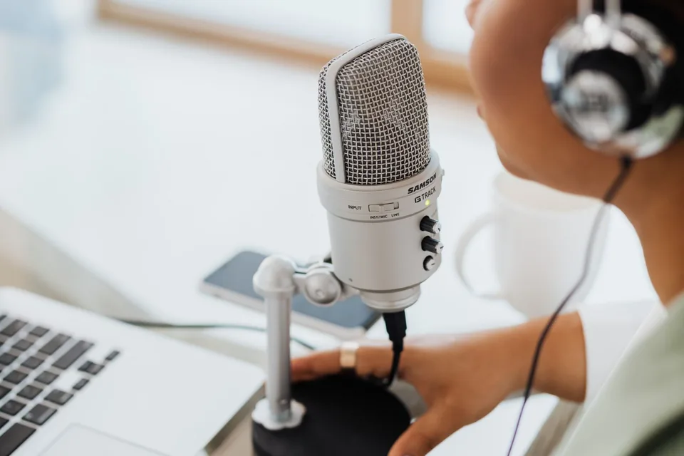Person wearing headphones humming a steady note about 20 cm from a desktop USB microphone next to a laptop
