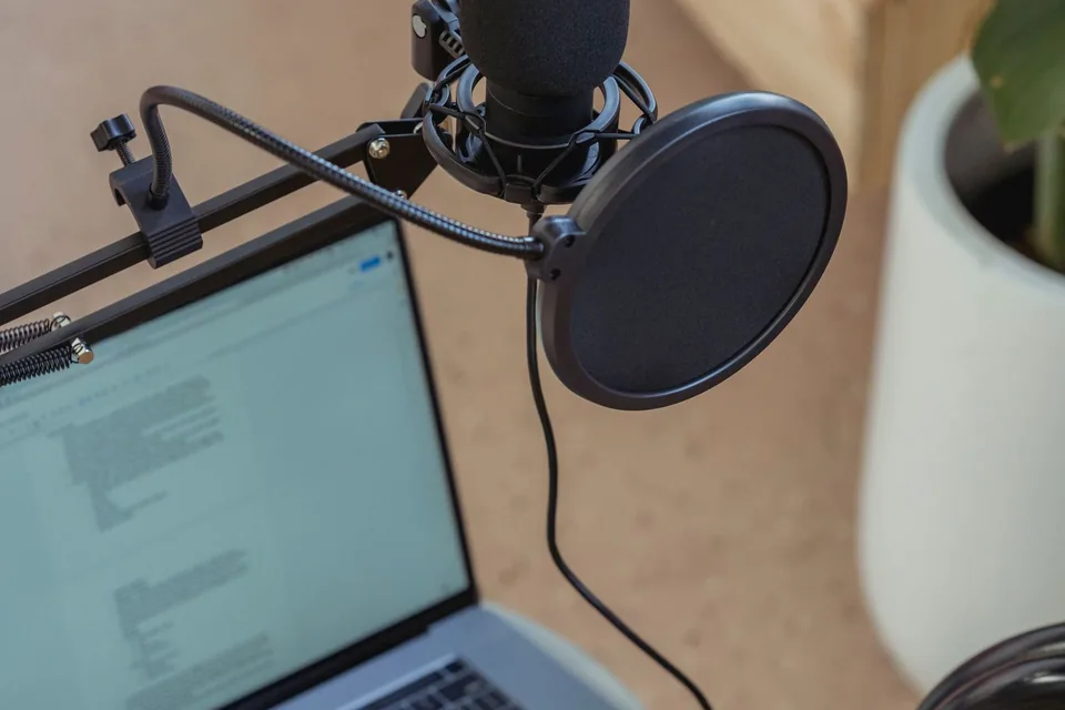 USB condenser microphone with a pop filter on a desk arm in front of a laptop, a simple home setup for pitch practice