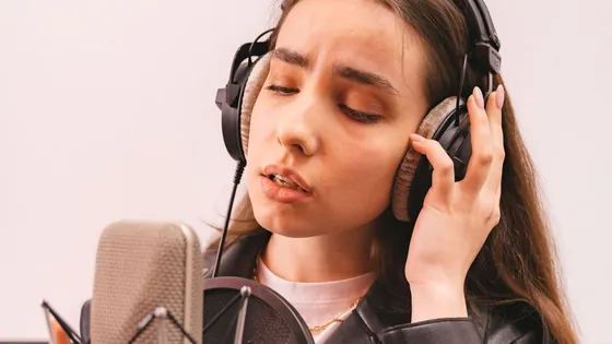 Young woman with headphones humming a note into a studio microphone to find out what note she is singing
