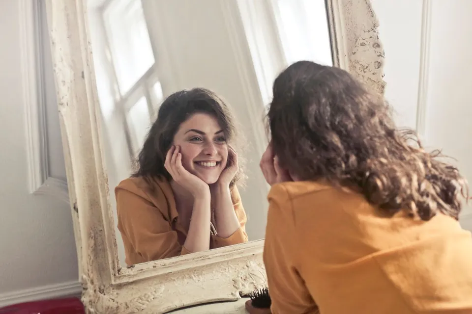 Woman smiling at her own reflection in a vintage framed mirror