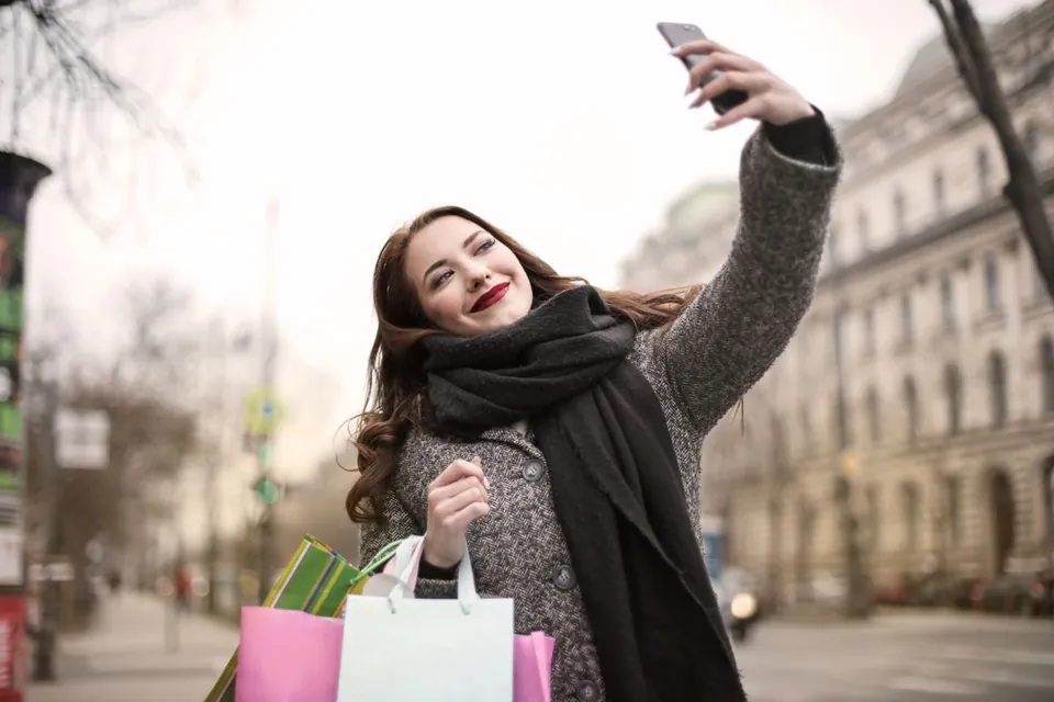 Woman holding up a smartphone at arm's length to take a selfie on a city street