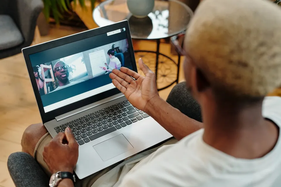 Man raising his open hand toward a laptop screen during a video call at home