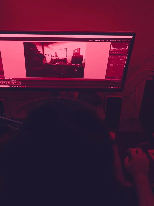 Person viewing a red-lit desktop monitor in a dark room