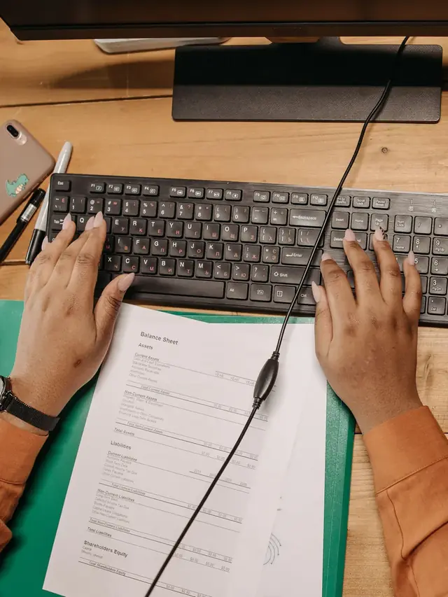 Person using a keyboard beside paperwork for reviewing results
