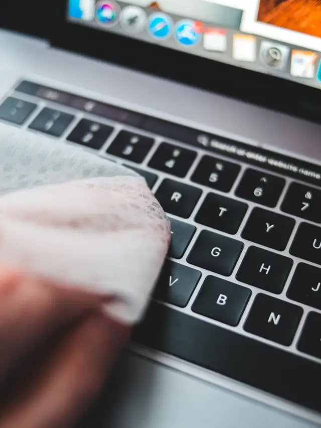 Person cleaning a computer keyboard with a soft wipe