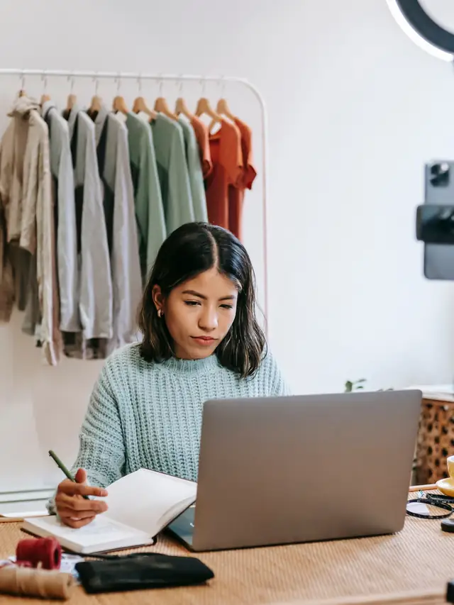 Woman writing in a notebook while using a laptop
