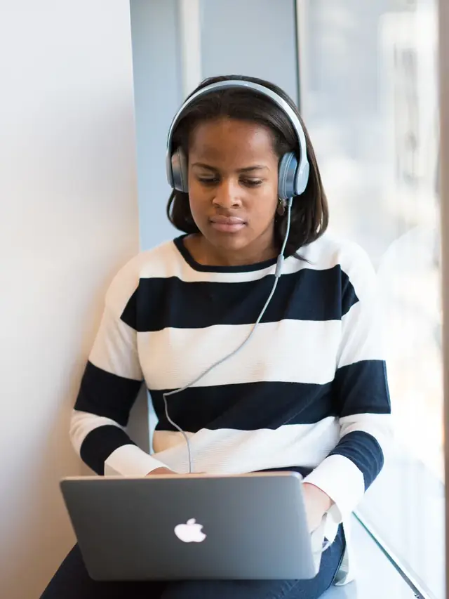 Focused woman listening through headphones while using a laptop