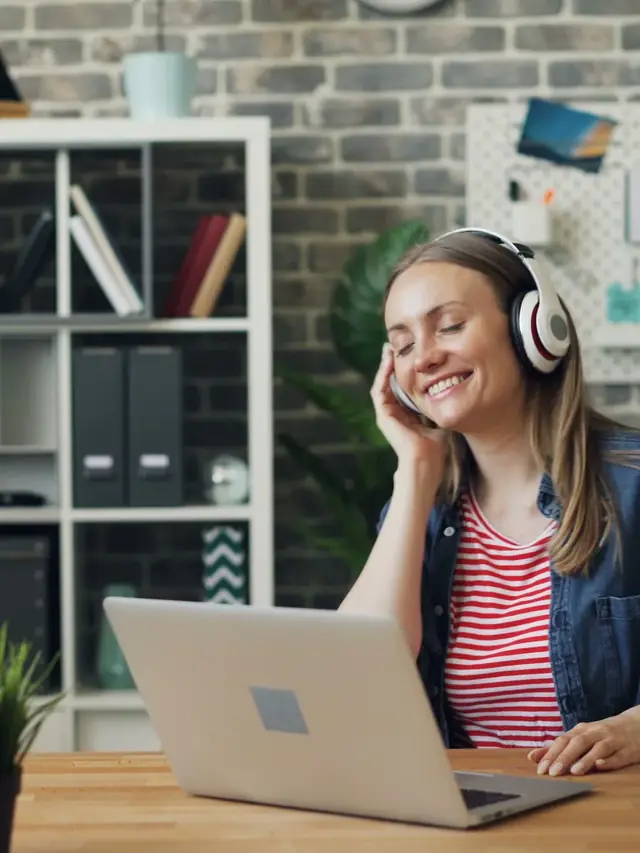 Woman wearing headphones while seated at a laptop in an office