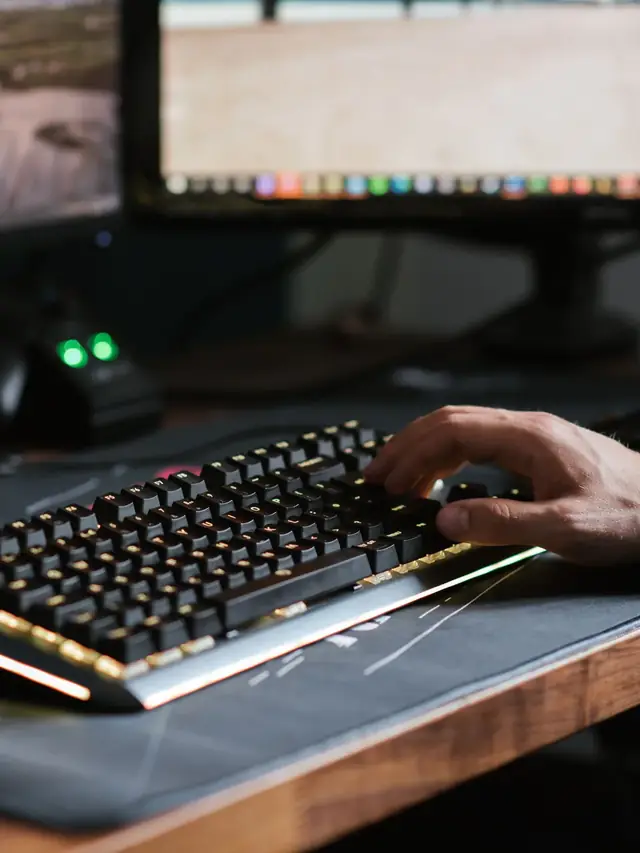 Person typing on a backlit keyboard in front of two monitors