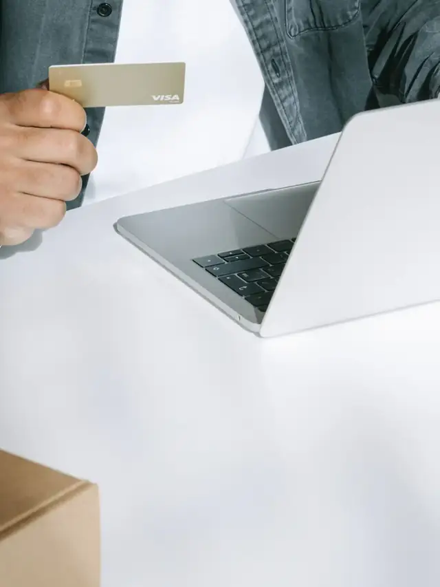 A person holding a payment card beside a laptop and boxes; stock illustration of comparing complete purchase costs